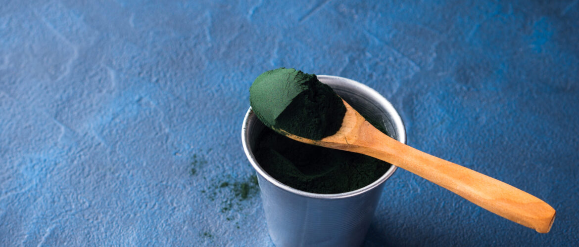 Spirulina super food powder in wooden spoon on blue background. Protein additive for smoothies